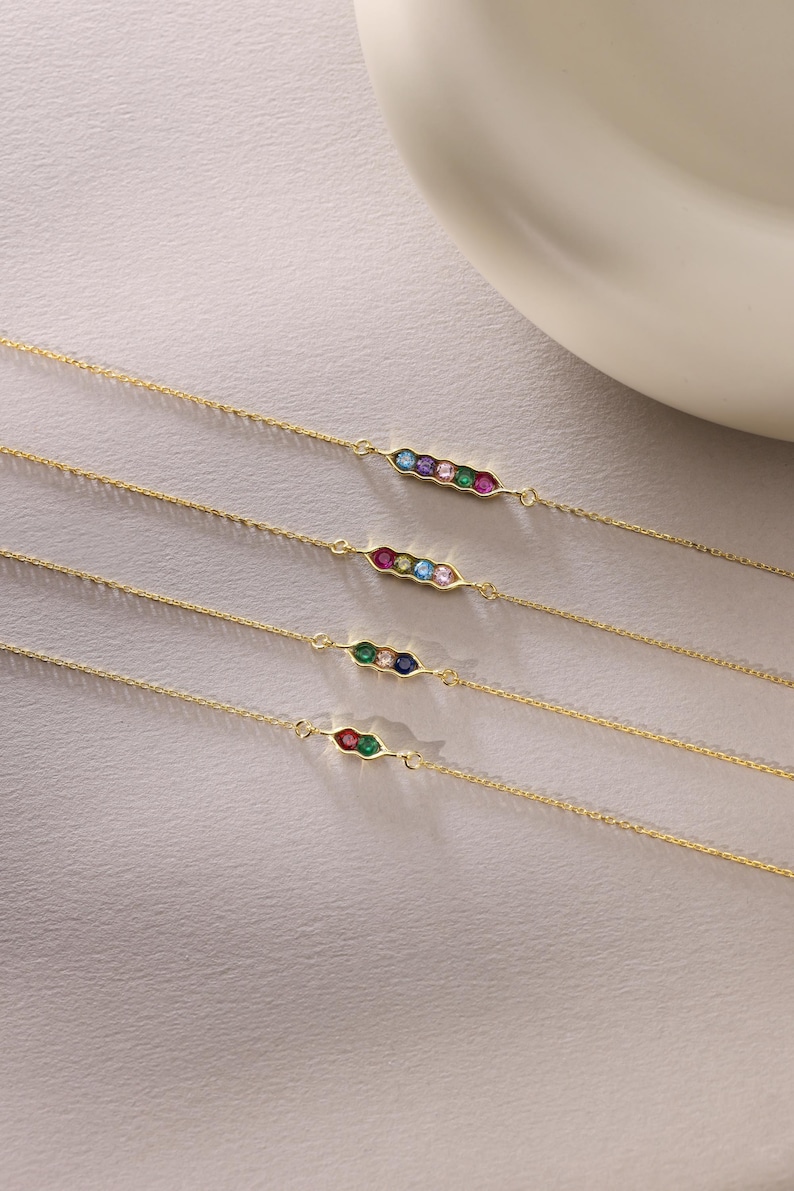 May include: Four gold chain bracelets with a pea pod design featuring colorful gemstones. Each bracelet has a different combination of gemstones, including red, blue, green, and pink.