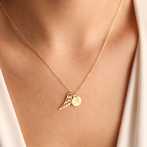 Puede incluir: Un collar de oro con una cadena delicada y un colgante que presenta un ala de &aacute;ngel individual y un peque&ntilde;o disco redondo con la letra 'A' grabada.