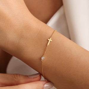 May include: A gold chain bracelet with a small cross charm and a single clear gemstone.