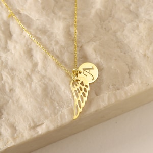 Puede incluir: Un collar de oro con una cadena delicada y un colgante que presenta un ala de &aacute;ngel individual y un peque&ntilde;o dije redondo con la letra "A" grabada en &eacute;l.