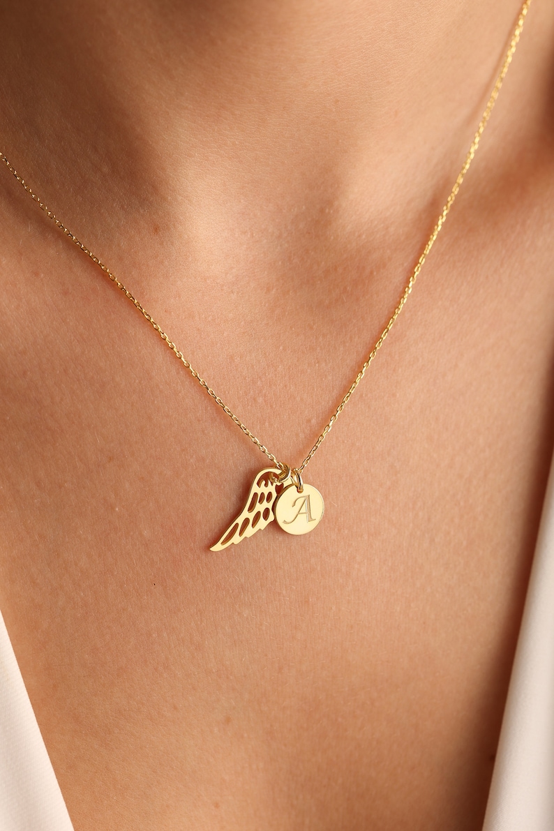 Puede incluir: Un collar de cadena dorada con un delicado dije de ala de &aacute;ngel y un peque&ntilde;o dije redondo con la letra 'A' grabada.