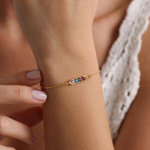 May include: A gold chain bracelet with a pea pod charm featuring five colorful gemstones.