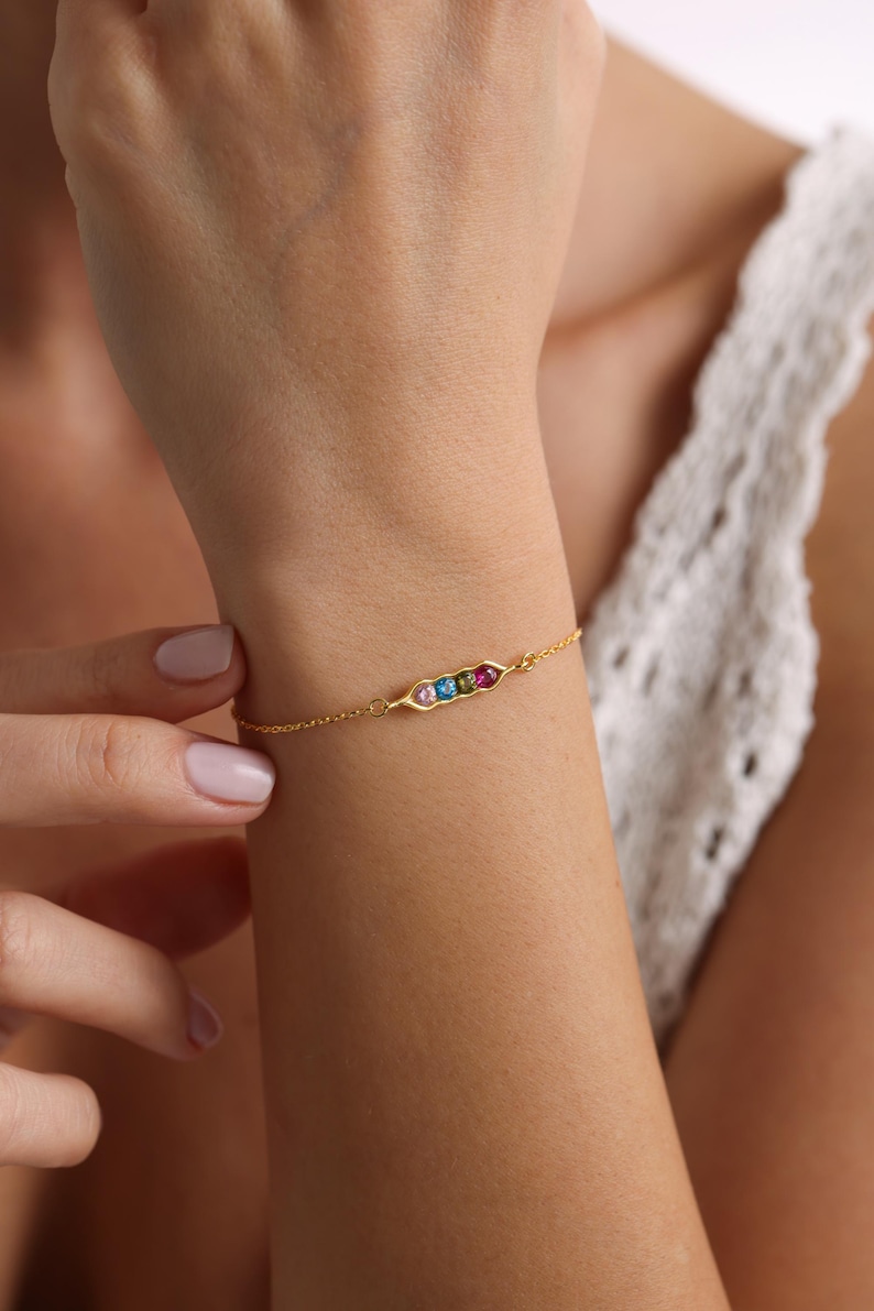 May include: A gold chain bracelet with a pea pod charm featuring five colorful gemstones.