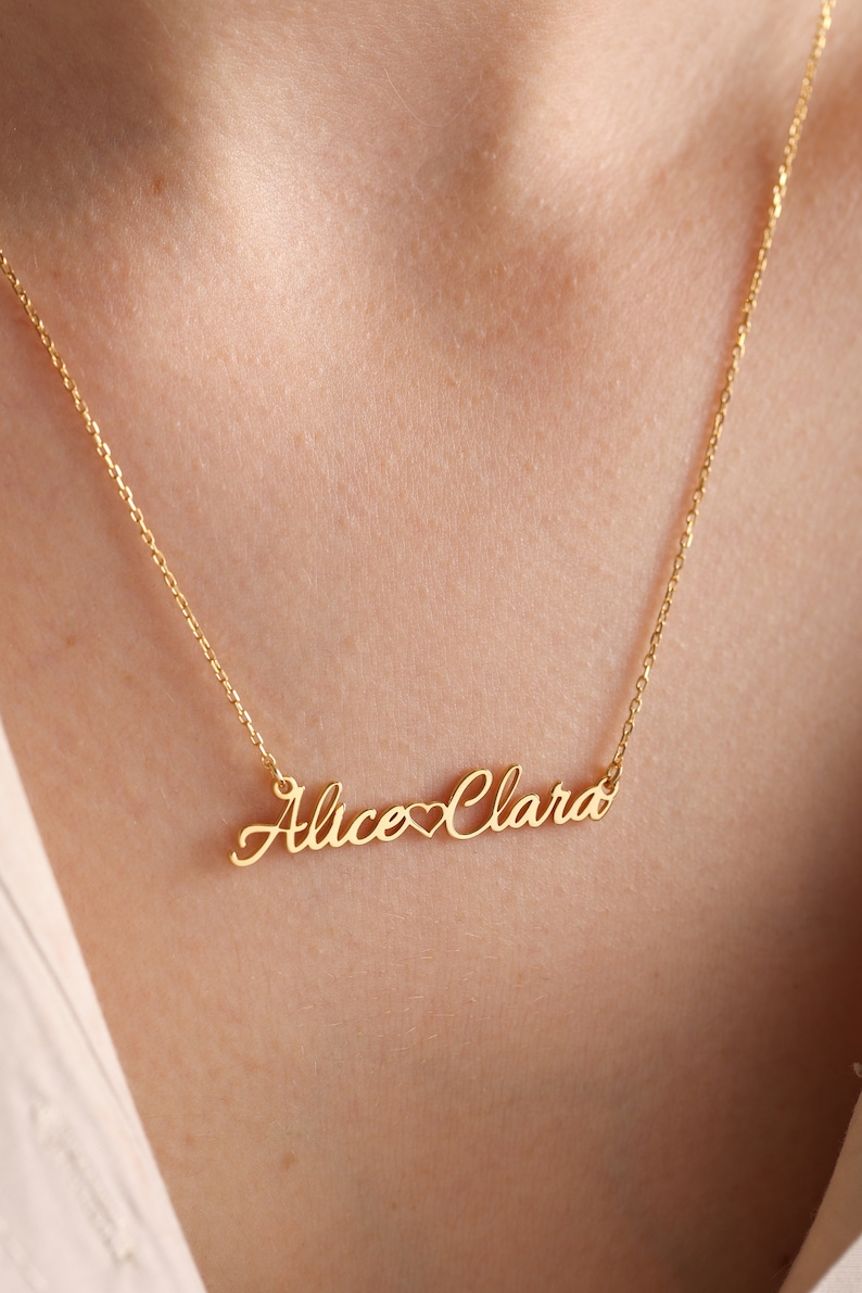 May include: Gold necklace with the names "Alice" and "Clara" connected by a heart symbol.