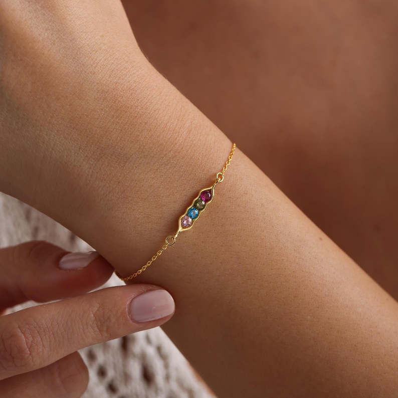 May include: A gold chain bracelet with a pea pod charm featuring five colorful gemstones.