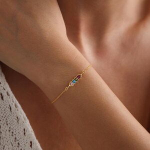 May include: A gold chain bracelet with a small, rectangular charm set with colorful gemstones. The charm is in the shape of a pea pod.
