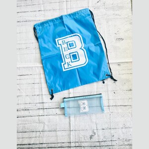 May include: A blue drawstring bag with a white "BECK" logo and a matching blue mesh pencil case with a white "B" logo.