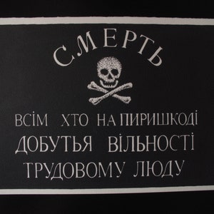 Könnte beinhalten: Ein schwarz-weißes Plakat mit einem Totenkopf und gekreuzten Knochen und dem Text "СМЕРТЬ ВСІМ ХТО НА ПІРІШКОДІ ДОБУТЯ ВІЛЬНОСТІ ТРУДОВОМУ ЛЮДУ" in kyrillischer Schrift.
