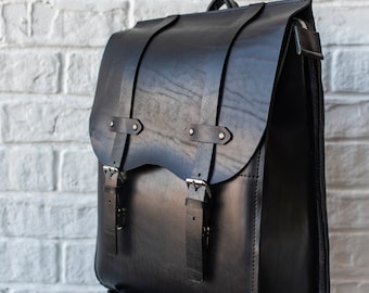Könnte beinhalten: Ein schwarzer Lederrucksack mit zwei verstellbaren Riemen und Schnallen. Der Rucksack hat einen Reißverschluss und eine Klappe mit einer Schnalle.