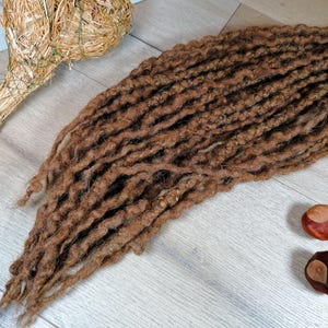 Könnte beinhalten: Ein Bündel brauner synthetischer Dreadlocks. Die Dreadlocks sind lang und dick und in einem lockeren, fließenden Stil angeordnet.