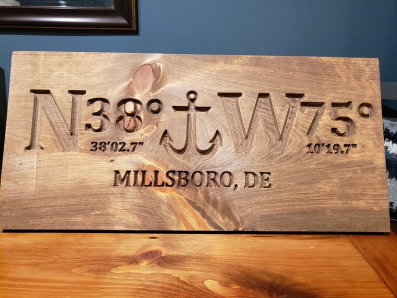 May include: A wooden sign with the coordinates N38&deg; 38'02.7" W75&deg; 10'19.7" and the text "Millsboro, DE" carved into it.