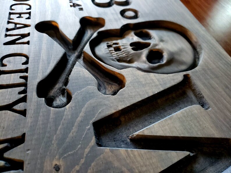 May include: A wooden sign with a carved skull and crossbones design. The sign reads "Ocean City MD" and has a distressed, rustic look.