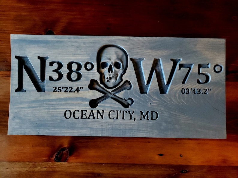 May include: A wooden sign with a carved skull and crossbones design. The sign reads "N38&deg; 25'22.4" W75&deg; 03'43.2" OCEAN CITY, MD".