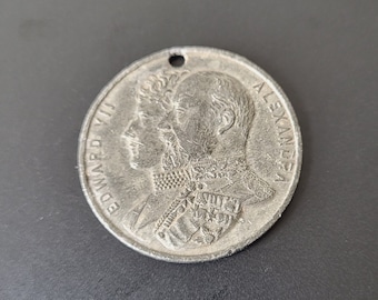 Könnte beinhalten: Ein silberfarbener Münzanhänger mit Profilen von zwei Männern. Die Münze trägt die Aufschrift "EDWARD VII" und "ALEXANDER". Oben befindet sich ein kleines Loch zum Aufhängen.