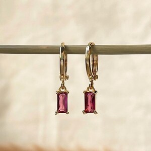 May include: A pair of gold hoop earrings with a dangling pink rectangular gemstone.