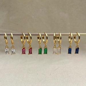 May include: A set of eight gold hoop earrings with dangling rectangular gemstones. The gemstones are in various colours, including white, red, green, and blue.