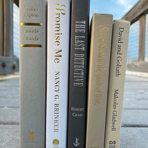 May include: A collection of five hardcover books with gold lettering on the spines. The books are arranged vertically from left to right. The titles are "Inside Inside" by James Lipton, "Promise Me" by Nancy G. Brinker, "The Last Detective" by Robert Crais, "Stronger Sheldon: The Sands of Time", and "David and Goliath" by Malcolm Gladwell.