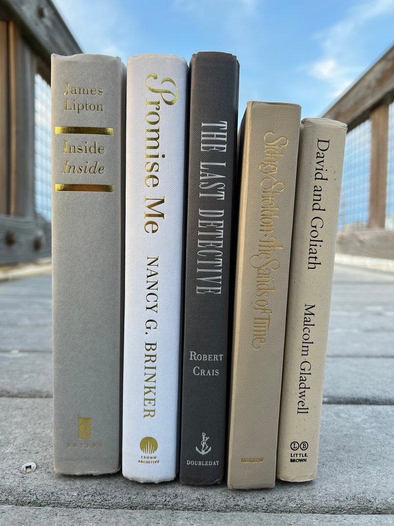 May include: A collection of five hardcover books with gold lettering on the spines. The books are arranged vertically from left to right. The titles are "Inside Inside" by James Lipton, "Promise Me" by Nancy G. Brinker, "The Last Detective" by Robert Crais, "Stronger Sheldon: The Sands of Time", and "David and Goliath" by Malcolm Gladwell.