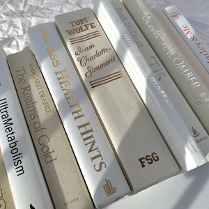 Peut inclure: Une collection de livres à couverture rigide, avec des titres et des auteurs variés. Les dos sont principalement blancs et beiges, avec des lettres dorées et argentées. On peut lire des titres comme "365 Health Hints" et "UltraMetabolism".