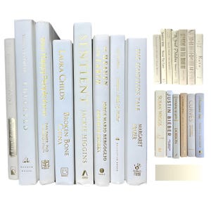 Könnte beinhalten: Eine Sammlung weißer Hardcover-Bücher mit goldener Schrift. Titel sind u.a. "Sentient" und "On Heaven and Earth". Die Bücher sind unterschiedlich groß und dekorativ angeordnet.
