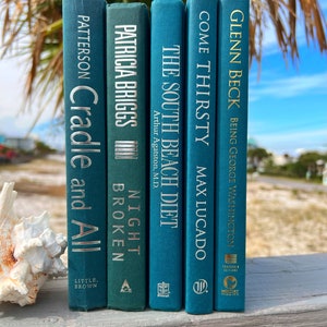 May include: A set of five teal blue hardcover books with gold lettering on the spines. The titles are "Cradle and All", "Night Broken", "The South Beach Diet", "Come Thirsty", and "Being George Washington".