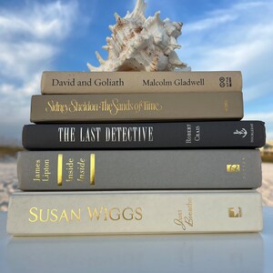 May include: A stack of five hardcover books with gold lettering on the spines. The books are arranged from top to bottom: David and Goliath, Sidney Sheldon - The Sands of Time, The Last Detective, Inside, and Susan Wiggs - Just Breathe.