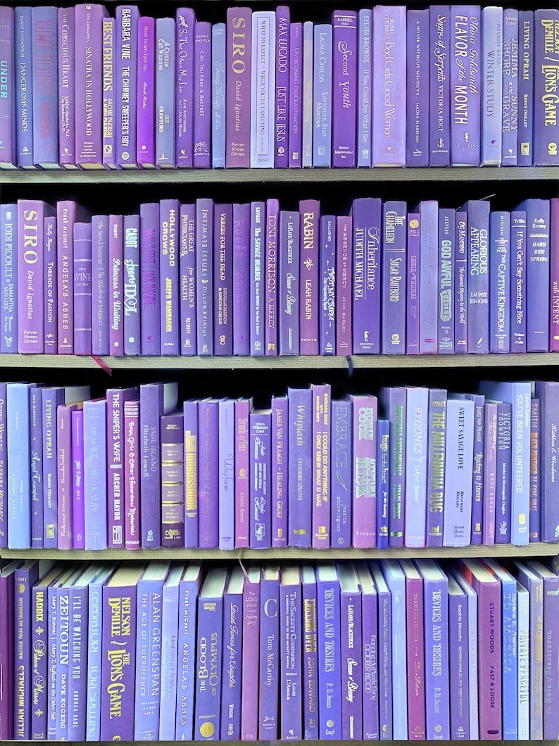 May include: A bookshelf filled with purple and lavender colored books. The books are arranged in rows and are all different sizes. The titles of the books are visible on the spines.