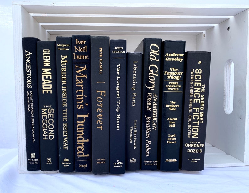 May include: A collection of black hardcover books with gold lettering on the spines. The books are arranged vertically in a white wooden crate. The titles of the books include "Old Glory", "The Passover Trilogy", "Liberating Paris", "Forever", "Martin's Hundred", "Murder Inside the Beltway", "The Second Messiah", "Ancestors", and "The Year's Best Science Fiction".