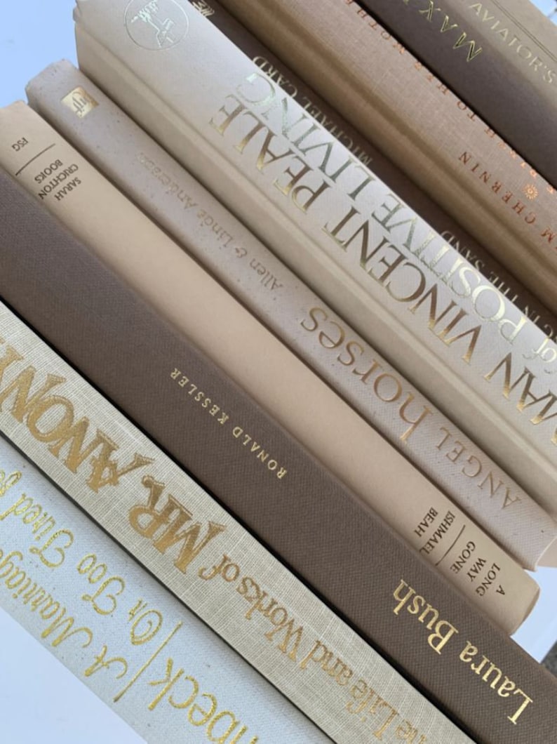 May include: A stack of books with beige and brown covers. The titles of the books are visible, including "Angel Horses", "Vincent Peale", "Man Positive Living", "A Long Way Gone", "Ismael  Beath", "Laura Bush", "Jo  Woods", "Mr. Anon", "Beck Or Too Tired", and "Sarah Crichton Books".