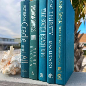 May include: A stack of five teal blue hardcover books with white text titles. The titles are "Cradle and All", "Night Broken", "The South Beach Diet", "Come Thirsty", and "Being George Washington".