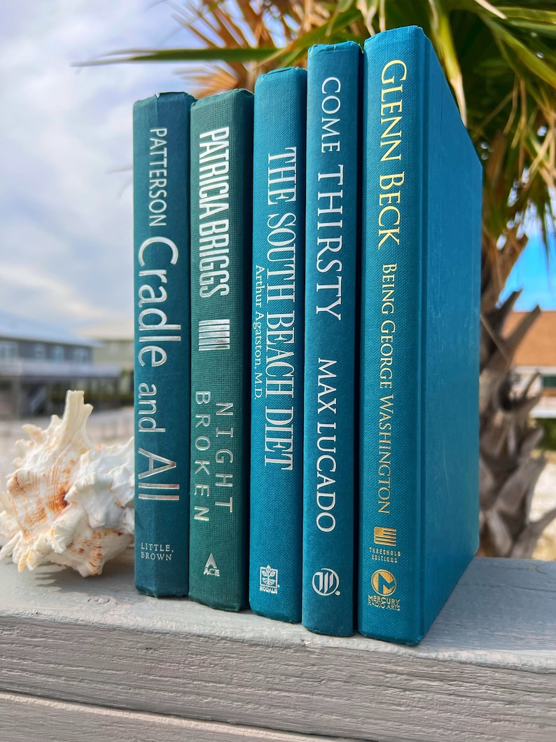 May include: A stack of five teal blue hardcover books with white text titles. The titles are "Cradle and All", "Night Broken", "The South Beach Diet", "Come Thirsty", and "Being George Washington".