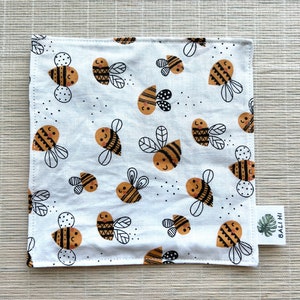 May include: White cotton fabric with a repeating pattern of black and brown bees. The fabric has a small tag with the text "BALI HI" on it.