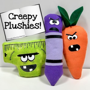 May include: A collection of handmade plushies with angry faces. The plushies include a green Frankenstein's monster, a purple crayon, and an orange carrot with green leaves. The text "Creepy Plushies!" is displayed on a book.