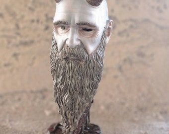May include: A silver-painted bust of a bearded man with horns. The horns are intricately carved with a pattern and are a dark brown color. The bust is on a brown base.