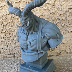 May include: A gray 3D printed bust of a monstrous creature with horns, a large mouth, and a stitched-up chest. The bust is on a square base.