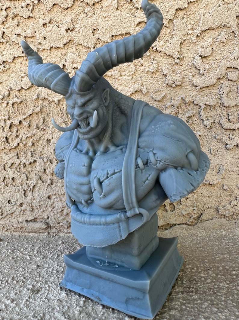 May include: A gray 3D printed bust of a monstrous creature with horns, a large mouth, and a stitched-up chest. The bust is on a square base.