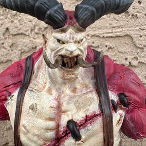 May include: A red and white painted bust of a demon with large black horns, a wide mouth, and a stitched-up chest. The demon has a menacing expression.