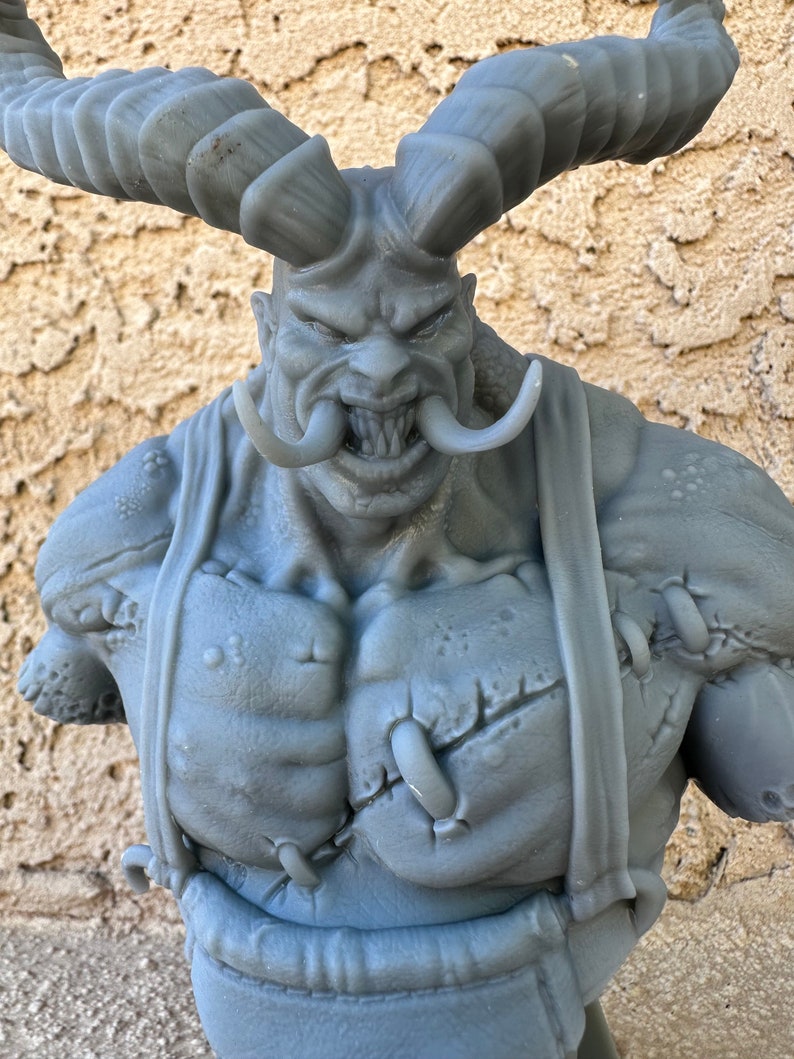 May include: A gray 3D printed bust of a demon with horns, a large mouth, and a stitched-up chest.