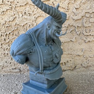 May include: A gray 3D printed bust of a demon with large horns and a fierce expression. The bust is on a square base.
