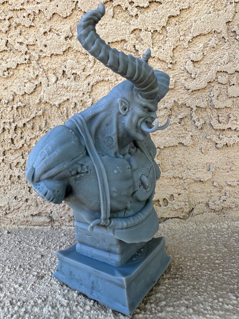 May include: A gray 3D printed bust of a demon with large horns and a fierce expression. The bust is on a square base.