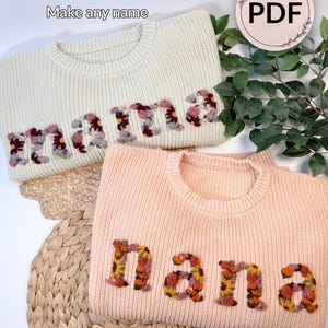 May include: Two crewneck sweaters, one cream and one peach, featuring embroidered letters. The cream sweater displays the word 'mama' in floral-patterned letters, while the peach sweater displays 'nana' in orange and yellow floral-patterned letters.