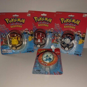 May include: Four Pokémon keychain toys in original blister packaging. Three feature characters Pikachu, Charmander, and Poliwag inside Poké Balls. The fourth is a Vaporeon figure in a circular container. All cards display the Pokémon logo.