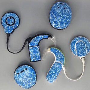 May include: Five blue and white patterned hearing aid devices with a water ripple design. The devices include a charging base, a behind-the-ear hearing aid, and a receiver.