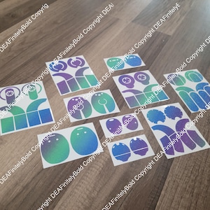 May include: A set of 10 vinyl stickers featuring a holographic, iridescent finish in shades of blue and green. The stickers are designed for customizing a pair of headphones. The stickers feature various shapes and designs, including circles, squares, and curved lines.