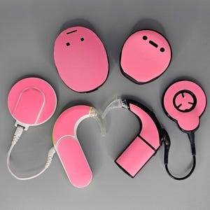 May include: A set of pink hearing aid components, including a receiver, a microphone, a processor, and a battery pack. The components are all made of a soft, flexible material and are designed to be comfortable to wear.