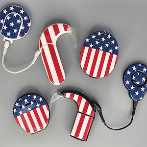 May include: Five hearing aid devices with American flag designs. The devices are in various shapes and sizes, including a round, a rectangular, and a curved shape. The devices are all white with red and blue stripes and stars.