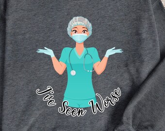 Pode incluir: Uma camisa de frio cinza escura com um gráfico de uma enfermeira usando uma touca cirúrgica, máscara facial e luvas. O texto "I've Seen Worse" está impresso abaixo da enfermeira.