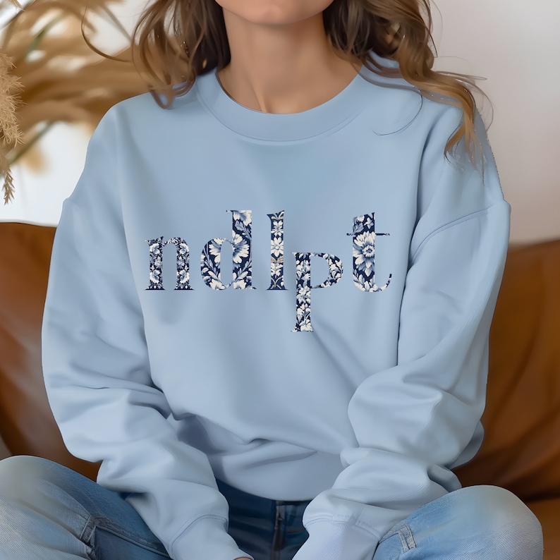 May include: A light blue sweatshirt with a floral pattern spelling out the word "ndipt".
