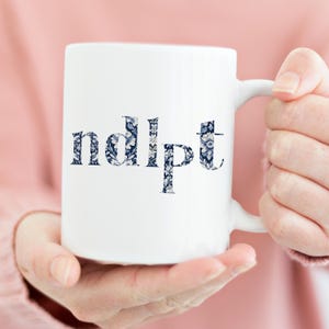 May include: White ceramic mug with a blue and white floral pattern spelling out the word "ndlpft".