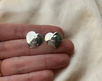 May include: A pair of silver heart-shaped earrings with a layered design. The earrings are small and delicate.